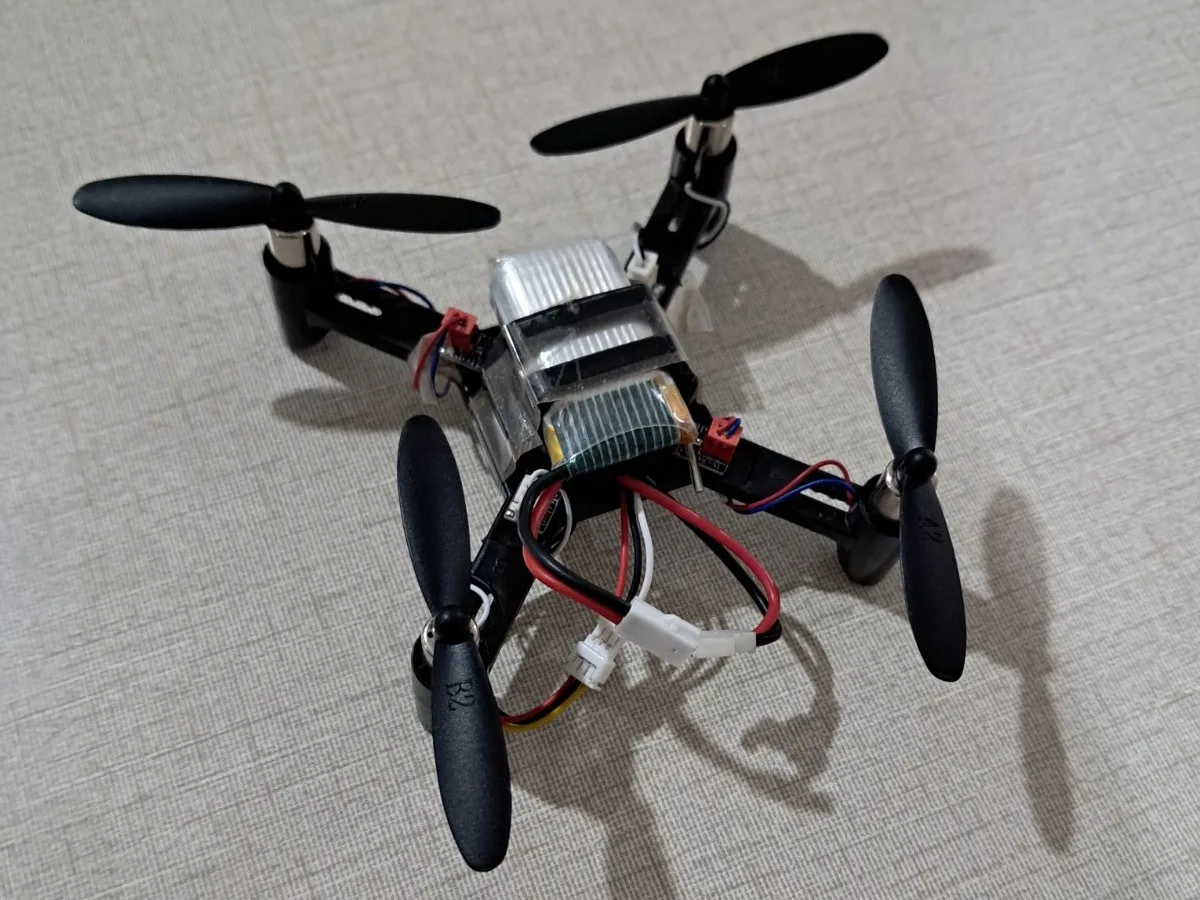 A small home-built quadcopter with its battery and wiring exposed, sitting on a table